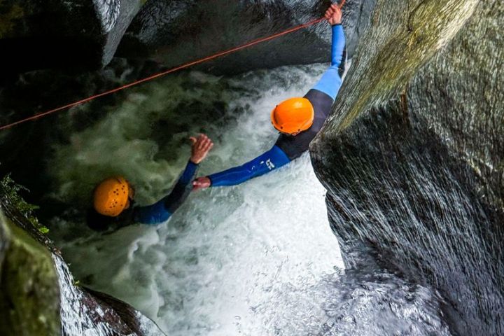 Two people canyoning with helmets and ropes through narrow water passageway.