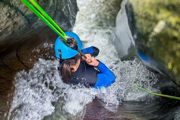 Person with blue helmet canyoning in a narrow water stream.
