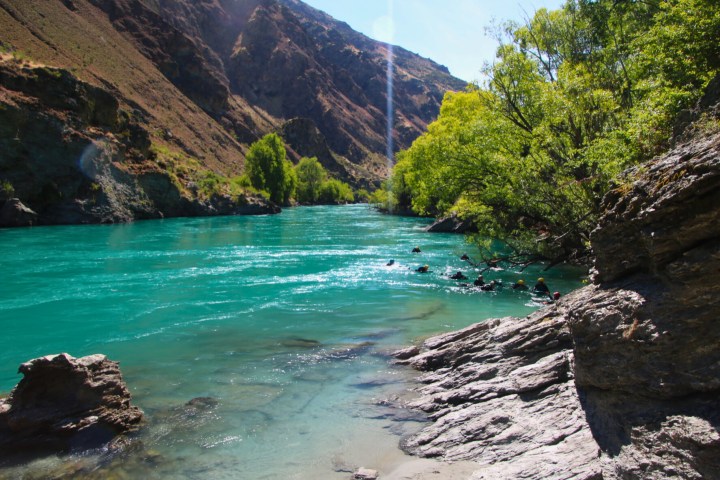 Clear turquoise river flowing through rocky landscape with trees and mountains.