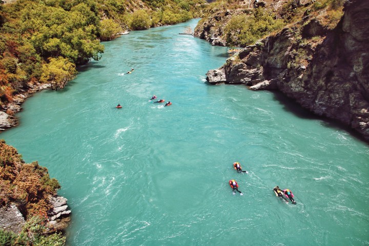 People kayaking on a winding turquoise river surrounded by lush greenery.