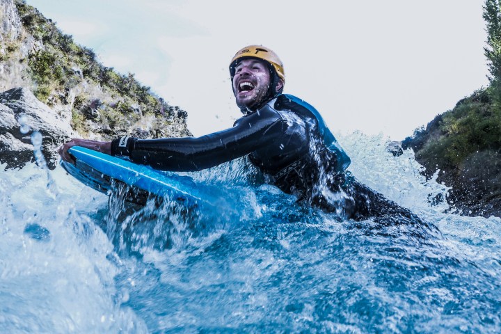 Person wearing a helmet and wetsuit rides a blue riverboard in rushing water.